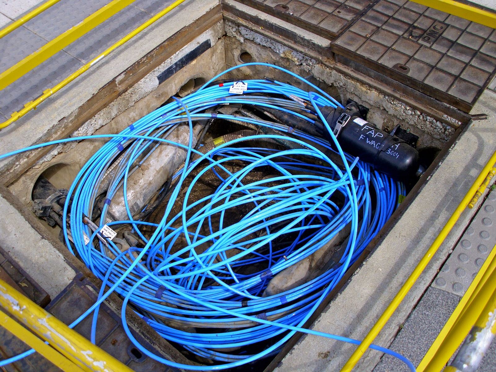 A pavement access pit opened to show coiled fibre-optic cable in a service duct.